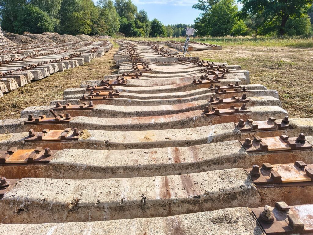 Disused railway sleepers lined up in a sunny, open field with lush greenery.