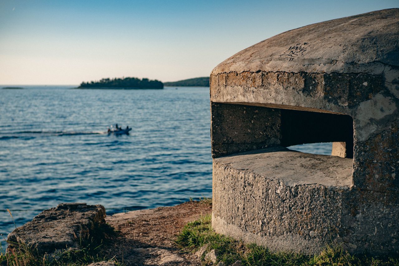 Historic bunker on Adriatic coast with view of distant island and boat in Rovinj, Croatia.